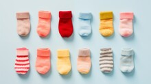 A Row Of Tiny Baby Socks In Various Patterns And Colors, Creating An Endearing Visual On A Light Blue Surface.