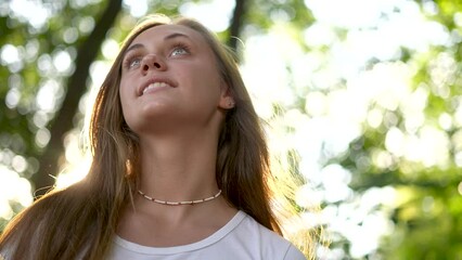 Wall Mural - beautiful girl smiling. inner beauty and love for nature concept. beautiful woman stands in a park lifestyle outdoors in a white T-shirt and smiles, face close-up, sun glare on the background