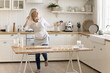 © fizkes - Cheerful mature woman in apron dancing in the kitchen, listen favorite music, moving, feel carefree, prepare holiday cake for family, enjoy culinary hobby alone at home. Domestic activity, cooking