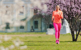 Fototapeta  - Sportive girl running in park on spring day in front of blossom