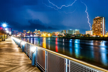 Wall Mural - Wilmington skyline by night reflected in Christiana River, along Jack Markell boardwalk trail, during a lightning storm. Wilmington is the largest city in the state of Delaware.