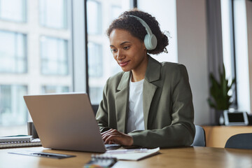 Wall Mural - A woman with headphones is at a table using a laptop computer