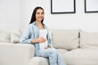 © New Africa - Happy pregnant woman on sofa at home, space for text