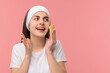 © New Africa - Young woman with headband washing her face using sponge on pink background, space for text