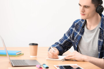 Wall Mural - E-learning. Young man taking notes during online lesson at table indoors.