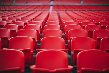 Football stadium with empty seats. Outstanding empty red plastic chair at soccer arena. Row of unoccupied bench at sports stadium. Reserved seating for football game concept. Outdoor audience chairs