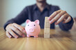 © abcvector - Person building a tower from wooden blocks beside a piggy bank, symbolizing financial planning and saving