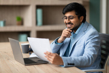 Aufkleber - Contented Indian businessman looks through papers engrossed in work indoor