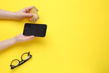 Canvas Print - Online payment. Woman with smartphone, credit card and glasses on yellow background, top view. Space for text