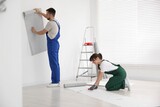 Fototapeta Panele - Woman applying glue onto wallpaper while man hanging sheet indoors