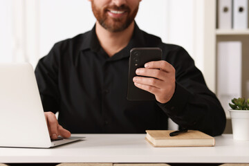 Poster - Smiling man using smartphone at table in office, closeup