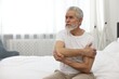 Arthritis symptoms. Man suffering from pain in elbow on bed at home