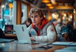 A young student with curly hair and a puffer jacket is focused on his laptop, working studiously amidst the lively atmosphere of an urban coffee shop, illuminated by warm bokeh lights