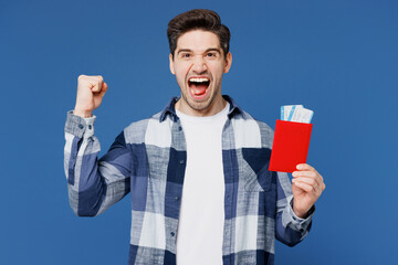 Poster - Traveler man wear shirt casual clothes hold passport ticket do winner gesture isolated on plain blue background. Tourist travel abroad in free spare time rest getaway. Air flight trip journey concept.