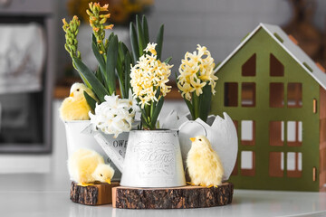 Wall Mural - Happy Easter. Spring yellow hyacinth flowers in an egg-shaped vase, chicken chicks on a white table. In the background is a white Scandinavian-style kitchen. Easter decor in the house.