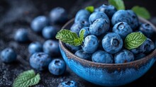  a blue bowl filled with blueberries with green leaves on the top of the bowl and blueberries on the bottom of the bowl.