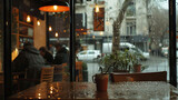 Fototapeta Uliczki - A cozy coffee shop with a view of the rainy street outside. The warm glow of the lights inside the shop contrasts with the cold, wet weather outside.
