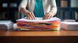 Close-up of a woman's hands organizing a large stack of documents and folders on a wooden desk