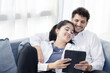 © charnsitr - Happy couple sits on a couch enjoy watch movie on tablet