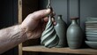 a hand holding a piece of pottery in front of a set of vases on a shelf with a rope.