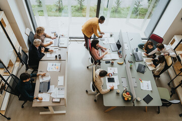 Cross generational coworkers collaborating on innovative ideas for successful teamwork in a startup office. Top view shot.