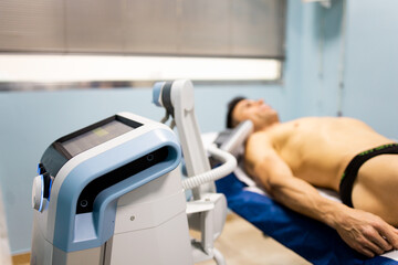 An adult man undergoes super inductive system therapy for recovery from trauma and rheumatic pathologies in a physiotherapy clinic.The machine is in the foreground. Super Inductive System, SIS.