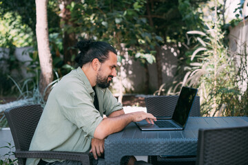 Wall Mural - A male freelancer, a digital nomad, remotely works on a laptop in the hotel garden.