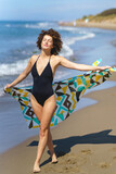Fototapeta  - Stylish woman in swimsuit stretching hand on sandy beach