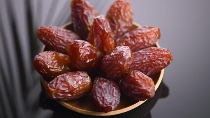 Poster - Dates fruit. Date fruits with palm tree leaf reflections on black background. Heap of Medjool dates rotating in a wooden bowl close up. Tasty healthy food