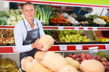 Sticker - Male supermarket worker standing in salesroom with pumpkin in hands.