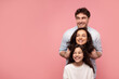 © Home-stock - Happy family, mother father and daughter posing, embracing while standing in line, looking together aside at copy space, posing on pink studio background