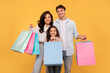 © Home-stock - European family of three shopping together, posing with colorful shopper bags and smiling over yellow studio background. Seasonal sales concept