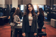 © Flamingo Images - Smiling businesswoman standing in an office lobby with coworkers holding a meeting in the background