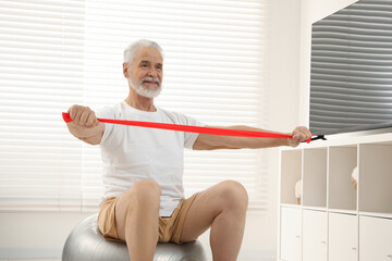 Poster - Senior man doing exercise with elastic resistance band on fitness ball at home