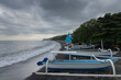 Black sand beach, fihsermen, boats and overcast sky at coastline of touristic Amed village in Bali island, Karangasm district