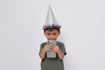 Wall Mural - Little small smiling happy Asian boy 2-3 years old wearing green t-shirt silver cone hat using mobile phone isolated on white background