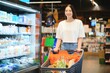 © Serhii - Happy young woman looking at product at grocery store. Smiling woman shopping in supermarket