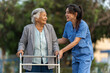 caregiver nurse support senior woman walking with walker in park