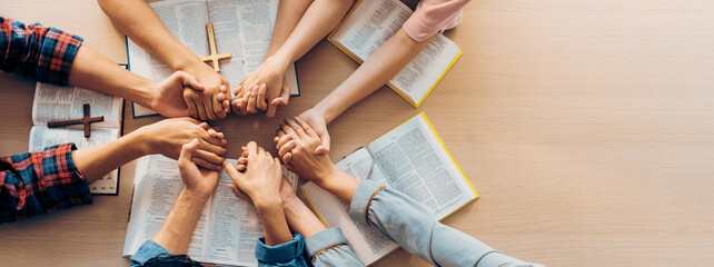 Poster - Cropped image of group of people praying together while holding hand on holy bible book at wooden church. Concept of hope, religion, faith, christianity and god blessing. Top view. Burgeoning.