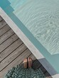 Female feet at poolside. Swimming pool with clear blue water with sunlight shadow reflections on waves. Minimal aesthetic summer vacation concept background