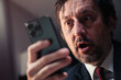 Shocked businessman reading text message on smartphone with surprised facial expression