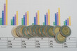 Przewrócony stos monet o nominale 5pln na tle wykresów słupkowych 