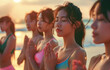 Group of young asian women doing yoga on the beach at sunrise, their eyes closed and hands in a prayer pose