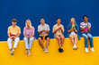 © Westend61 - Happy friends with colorful clothing sitting on yellow using their smartphones