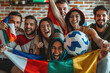 A group of happy friends were cheering for their football team, holding flags and playing with a soccer ball in the living room at home