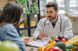 Male nutritionist providing dietary guidance to a female patient in a clinic filled with fresh produce