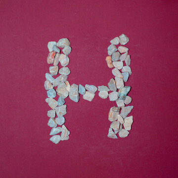 Letter H made of white stones. Creative alphabet concept on a red background. 