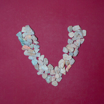 Letter V made of white stones. Creative alphabet concept on a red background. 