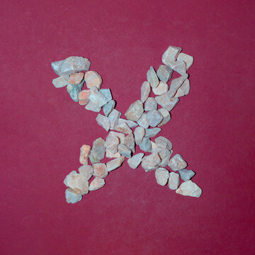 Letter X made of white stones. Creative alphabet concept on a red background. 