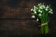 A vibrant, close-up image of a bouquet of snowdrops, bound with a simple twine, set against a dark walnut wood background.